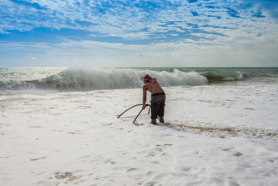 Man fishing while standing at beach against sky