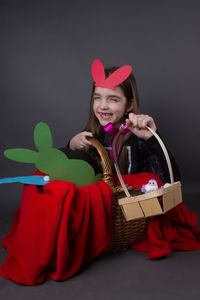 Portrait of smiling girl with costume rabbit ears sitting in basket against gray background