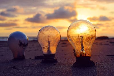 Close-up of abandoned light bulbs in sand at beach during sunset