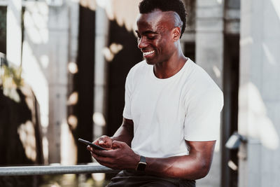 Smiling sportsman text messaging on smart phone sitting