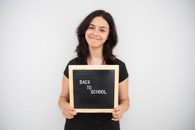 Portrait of young woman holding book against white background