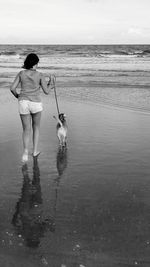 Full length of girl walking with dog on shore at beach