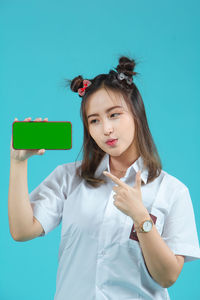 Portrait of smiling young woman using mobile phone against blue background