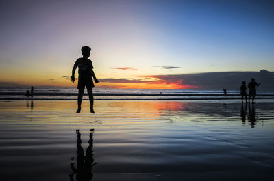 Silhouette woman standing on beach against sky during sunset