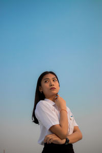 Portrait of a young woman standing against clear blue sky