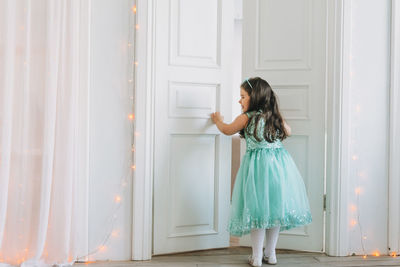 Cute happy little girl in mint fancy dress open door at bright room, birthday, christmas time