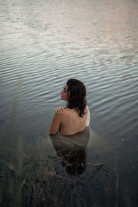 Back view of unrecognizable female traveler in fabric reflecting in pure lake water against trees during trip