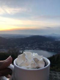 Close-up of whipped cream in coffee cup against sky during sunset