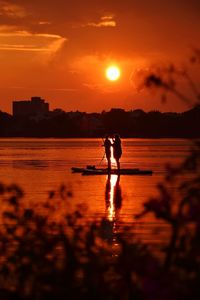 Silhouette men on shore against sky during sunset