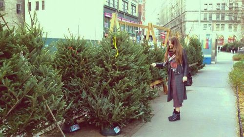 Young woman standing by plants in city