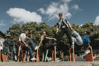 Low angle portrait of young male and female friends enjoying on metal bars at playground