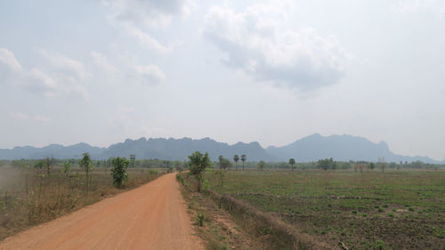 Dirt road amidst field against sky