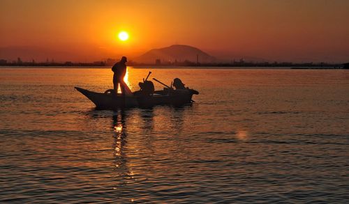 Silhouette men on boat in sea against sunset sky