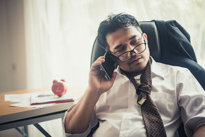 Businessman using phone while sitting on chair in office