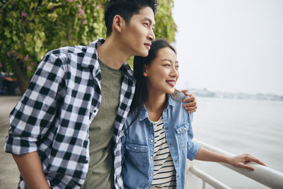 Young couple standing by railing against river