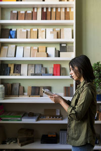 Female carpenter examining wooden samples by shelf at workshop