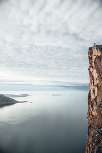 Low angle view of cliff by fjord with person standing on it