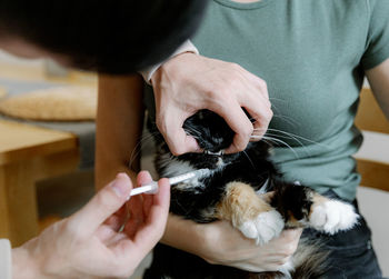 A young man gives medicine to a cat sitting in the arms of a girl.