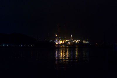 Illuminated city by river against sky at night