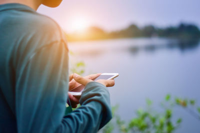 Midsection of man holding mobile phone against sky