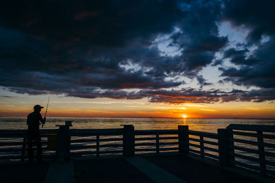 Silhouette man standing by sea against sky during sunset