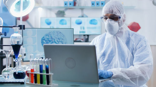 Scientist wearing mask and hazmat suit using laptop in lab