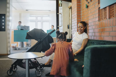 Smiling woman with daughter at sofa in waiting room of hospital