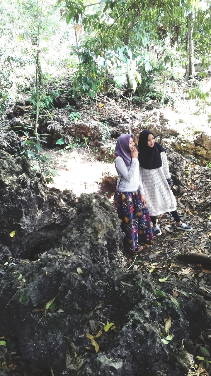 REAR VIEW OF WOMEN WALKING ON ROCK AGAINST TREES