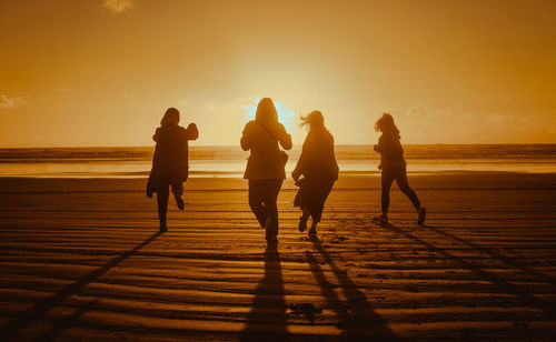 Silhouette people on beach against sky during sunset