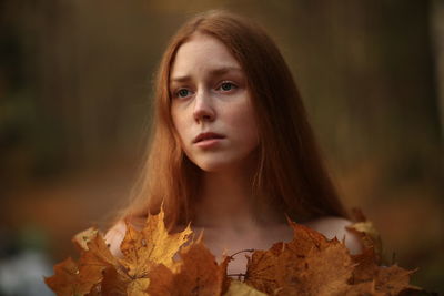 Close-up portrait of beautiful young woman with autumn leaves