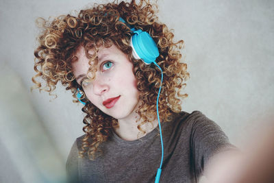 Portrait of woman with curly hair listening music against wall