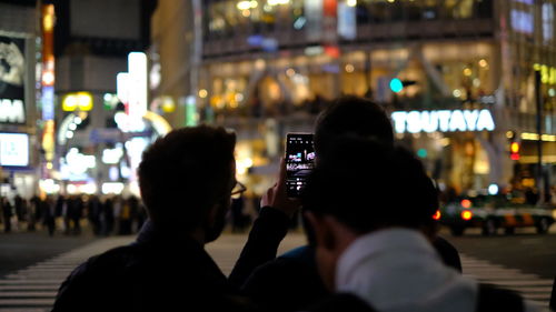 Rear view of man photographing in city at night