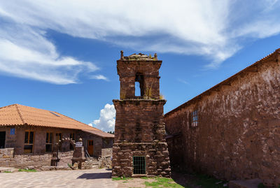 Low angle view of bell tower amidst houses against sky