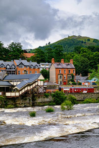 River flowing by houses against cloudy sky