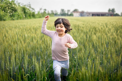 Girl with short hair in pink top runs with one hand up happily in wheat field