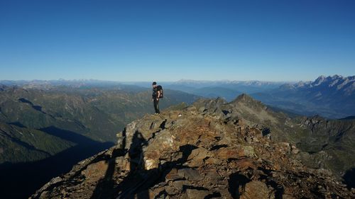 Mid distance view of hiker standing on rocky mountain against clear sky