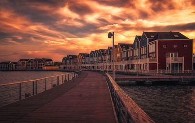 Bridge over river against houses during sunset