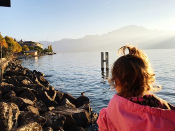 Rear view of girl by rocks in lake geneva