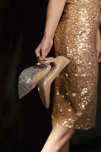 Woman holding shiny pair of heels against black background