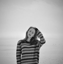 Young woman with eyes closed standing by sea against sky during winter