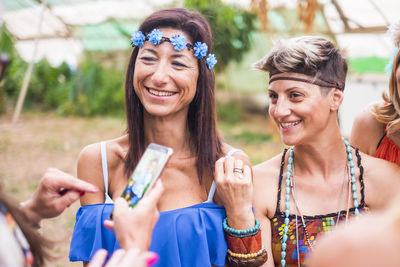 Cropped image of woman using mobile phone with smiling friends outdoors