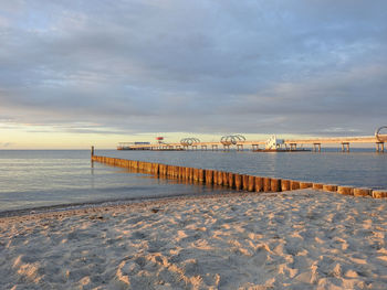 Pier on beach against sky during sunset