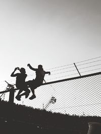 Boy and man sitting on fence against clear sky