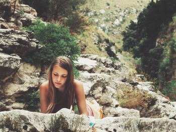 Young woman reading book while lying on rock in forest