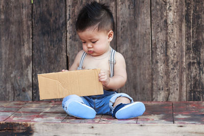 Cute baby boy holding cardboard while sitting on against on wooden table