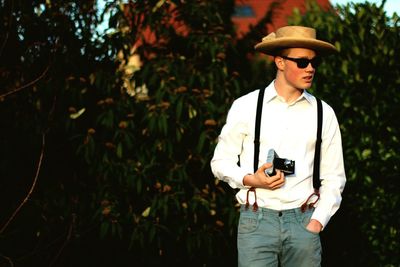 Handsome young man with hand in pocket holding retro camera