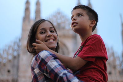 Portrait of smiling young woman carrying brother in city