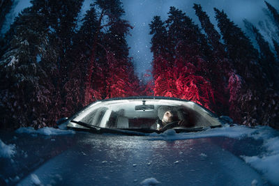 Mid adult man sitting in car seen through windshield at forest during winter