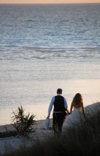 Rear view of couple walking towards sea at beach during sunset