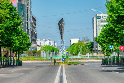 Road by trees and buildings in city against sky